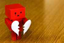 Red square-shaped robot with a tear drop. Holds a broken heart in his hiands