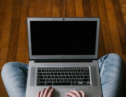 Person wearing jeans and a sweater sitting cross-legged on the floor with a laptop on their lap.